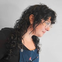 a woman with curly hair wearing glasses and an apron